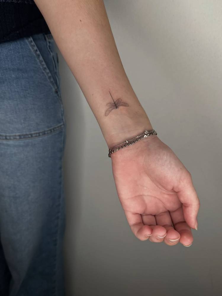 Tiny dragonfly tattoo placed on the wrist, fine line style.