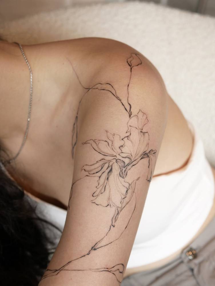 Iris flower tattoo in illustrative style located on the upper arm.