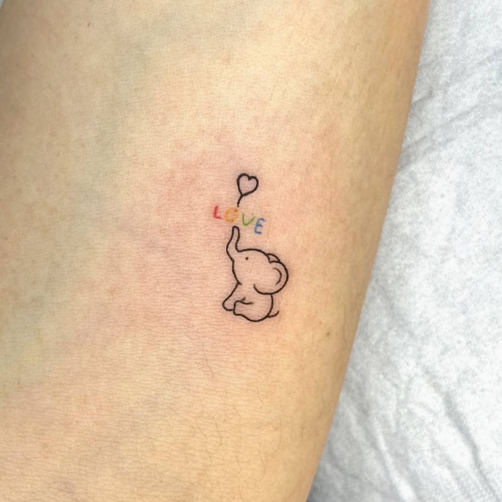 Tiny minimalistic elephant and word "love" tattoo located on the inner forearm.