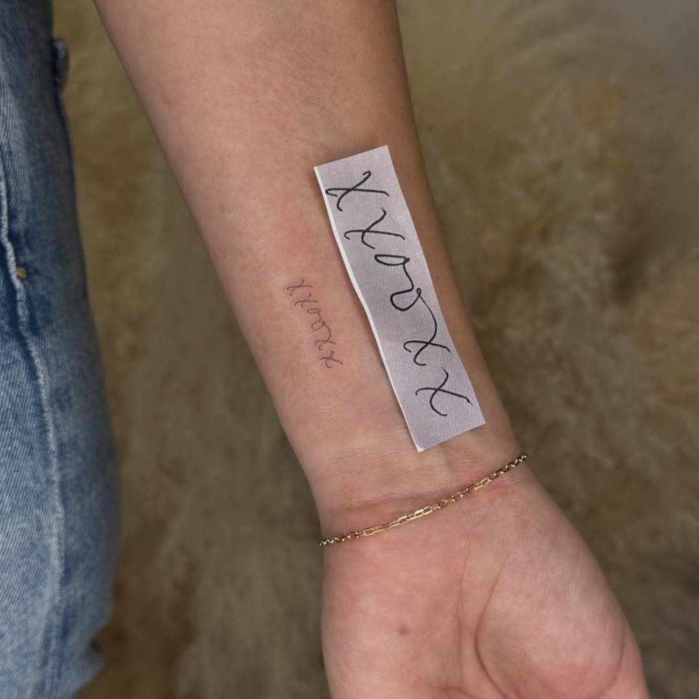 "XXOOXX" lettering tattoo in handwritten font located on the wrist.
