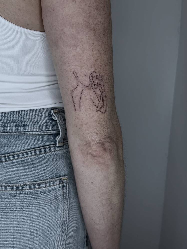 Pet hug tattoo in fine line style located on the tricep.