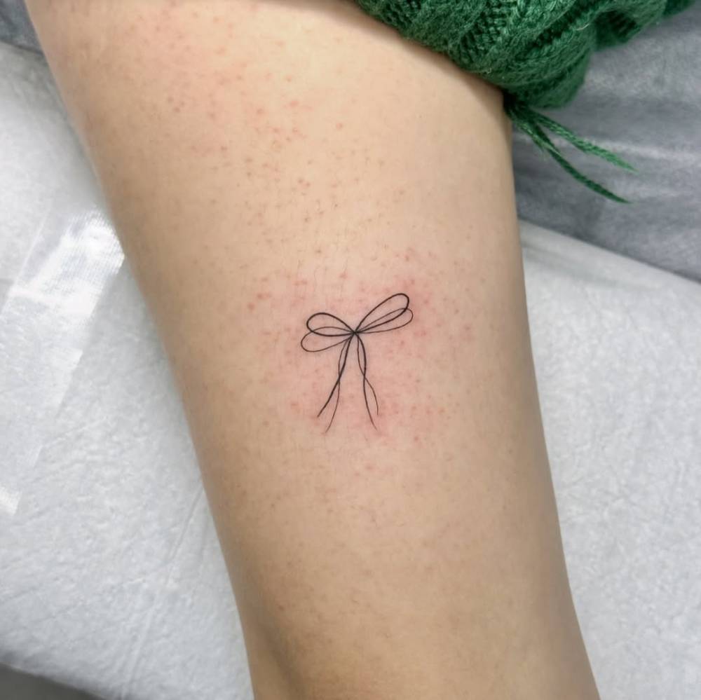 Bow tattoo in fine line style located on the upper arm.