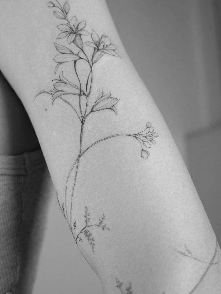 Lily flowers tattooed on the forearm, done in illustrative style.