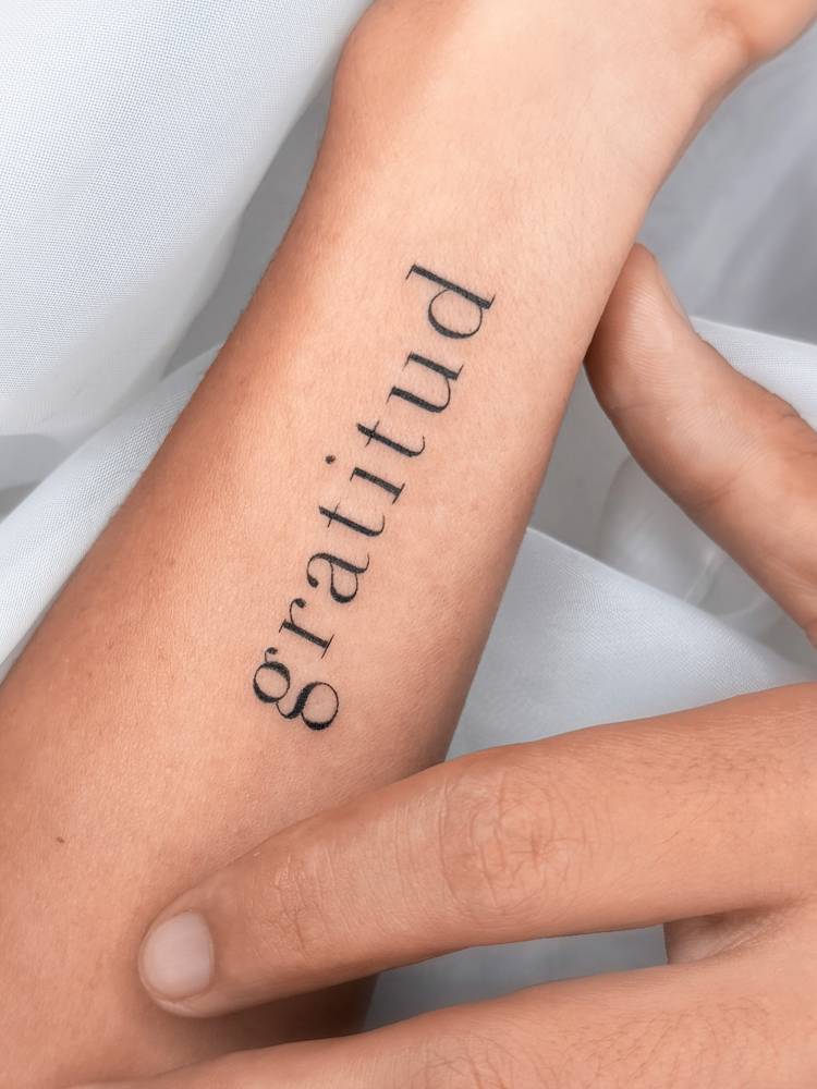Serif font word "gratitud" tattooed on the wrist.