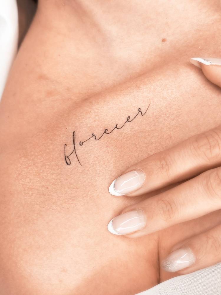 Handwritten font word "florecer" tattoo placed on the collarbone.