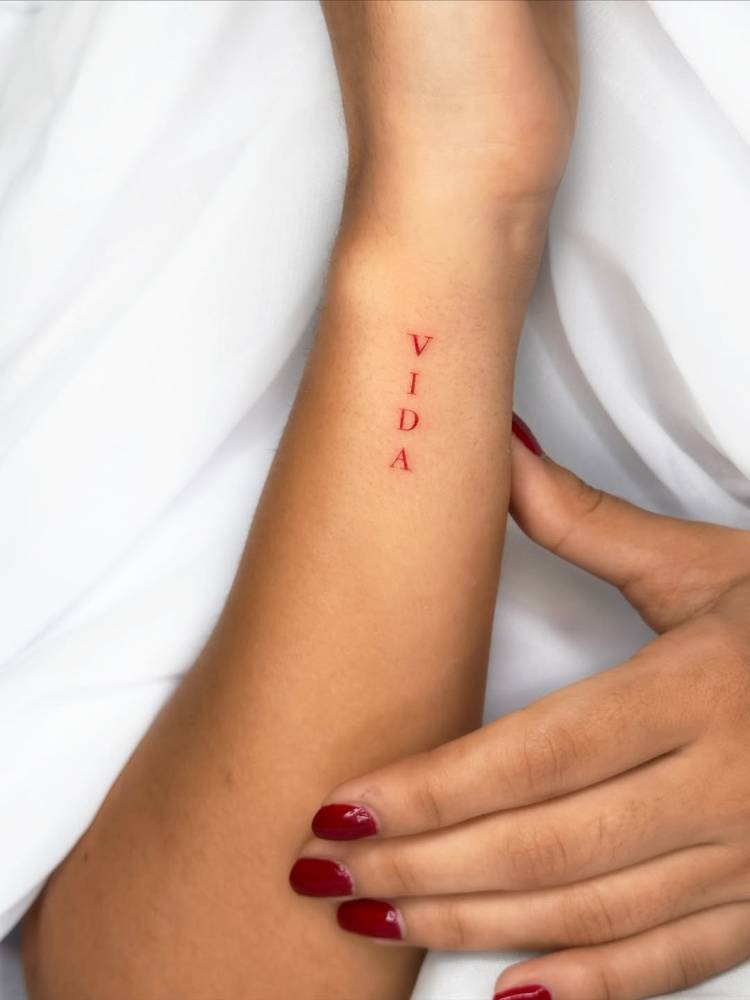 Word "vida" tattoo in red ink located on the wrist.