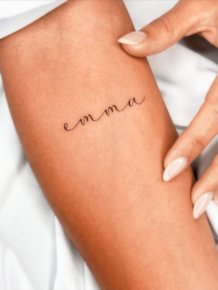 Script font name "Emma" tattoo done on the inner forearm.