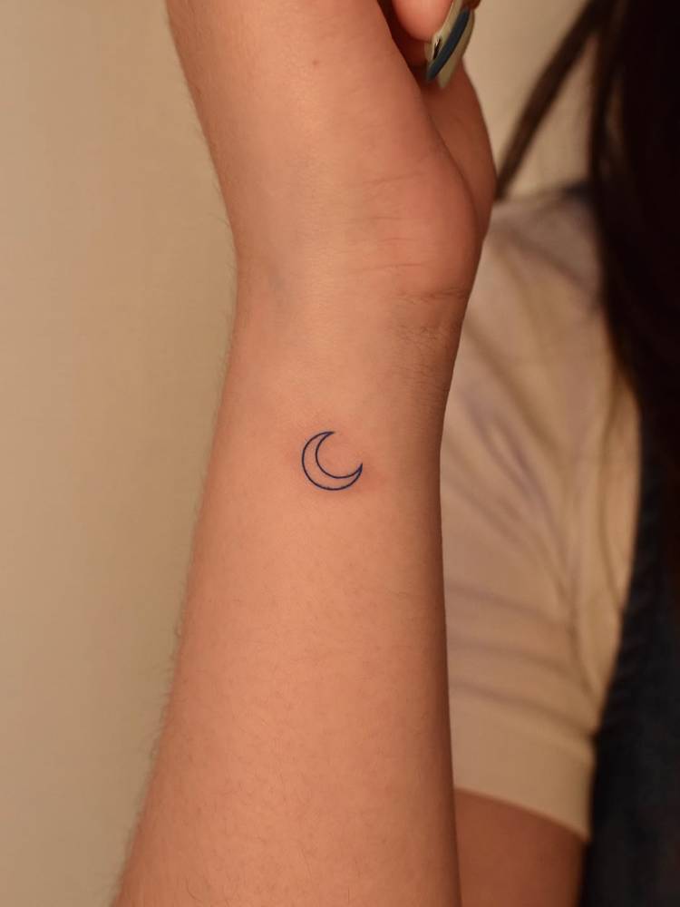 Micro crescent moon tattoo done on the wrist, minimalistic style.