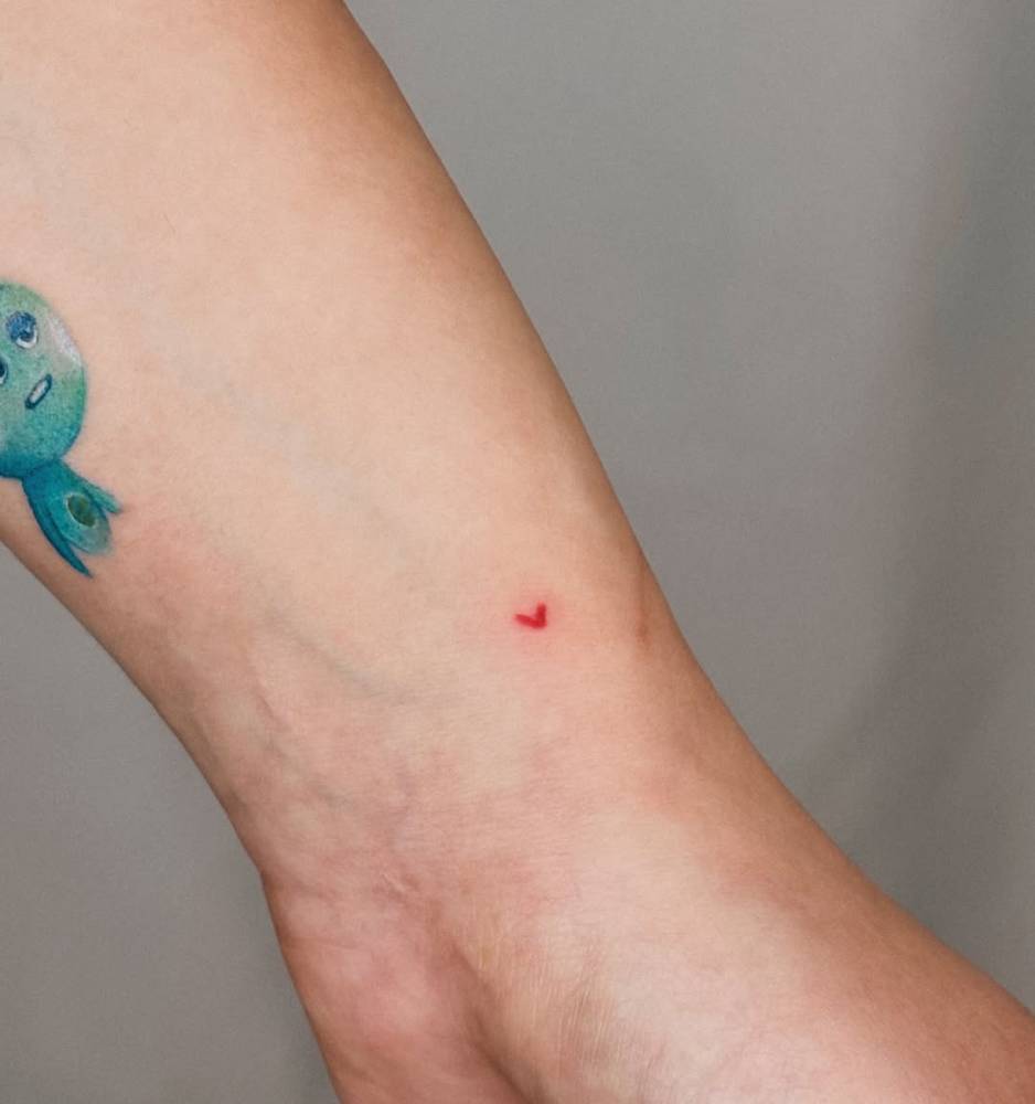 Micro red heart tattoo located on the wrist, done in minimalistic style.