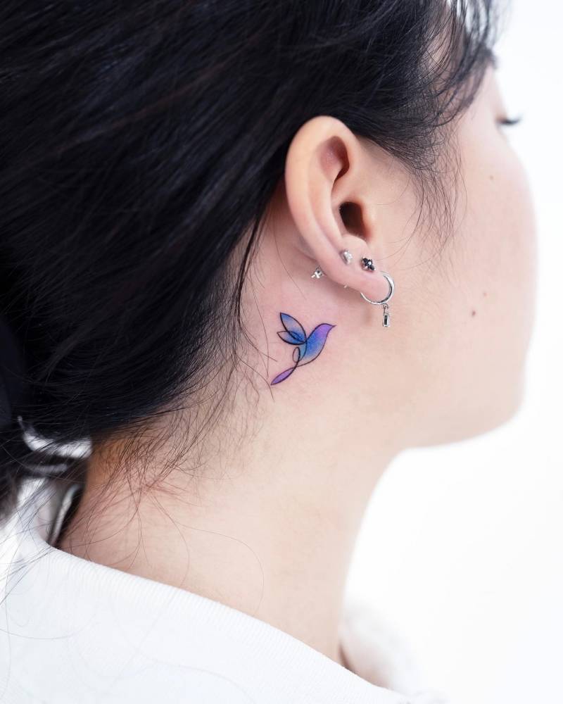 Watercolor style hummingbird tattoo located behind the ear.