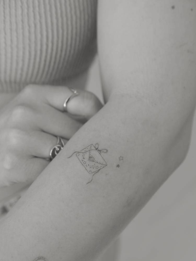 Small tattoo of a love letter in fine line style located on the forearm.