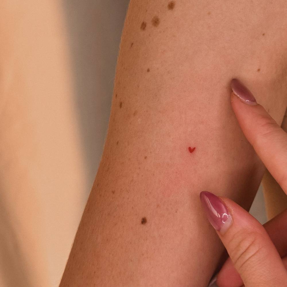Tiny red heart tattoo located on the inner forearm, minimalistic style.