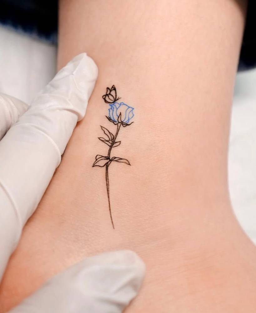 Sketch work style blue rose and butterfly tattoo located on the ankle.