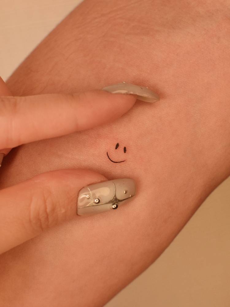Tiny smiley face tattoo located on the inner forearm, minimalistic style.
