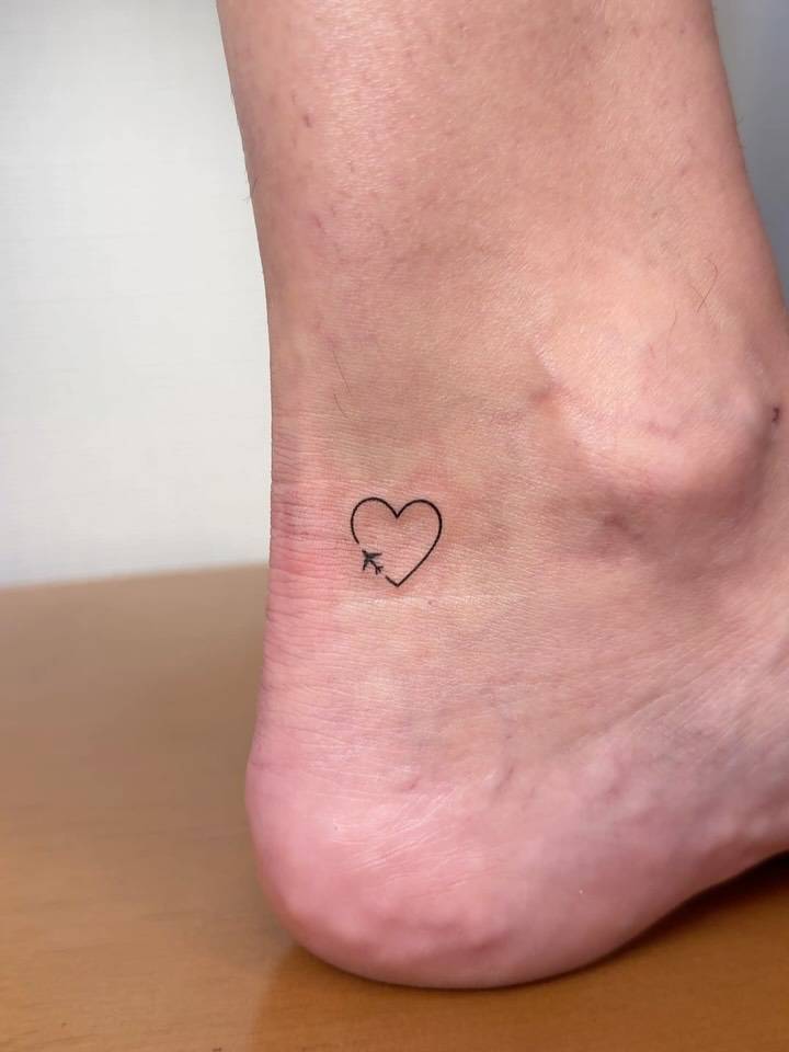 Airplane and heart tattoo in minimalistic style placed on the ankle.