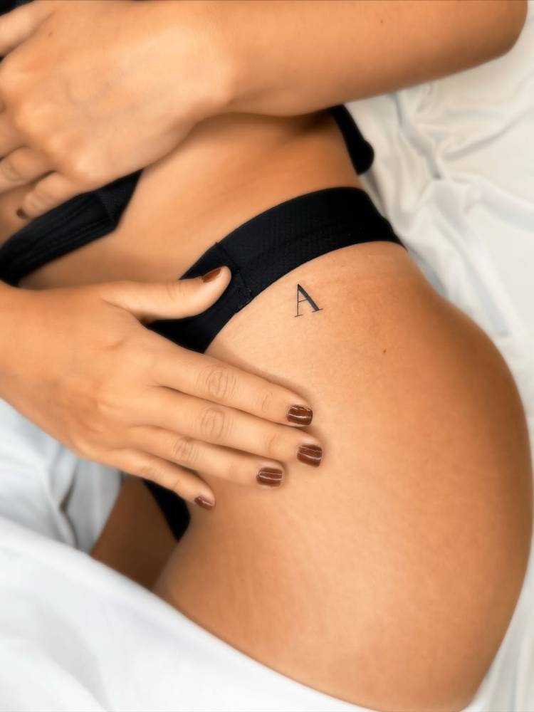 Serif font letter "A" tattoo located on the hip.