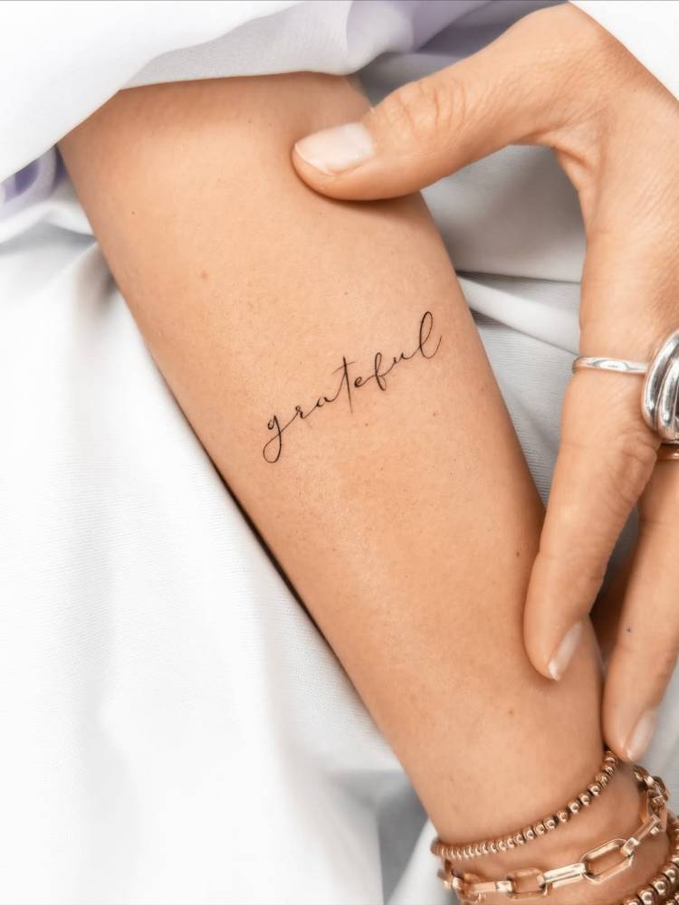 Lettering tattoo of the word "grateful" located on the forearm.