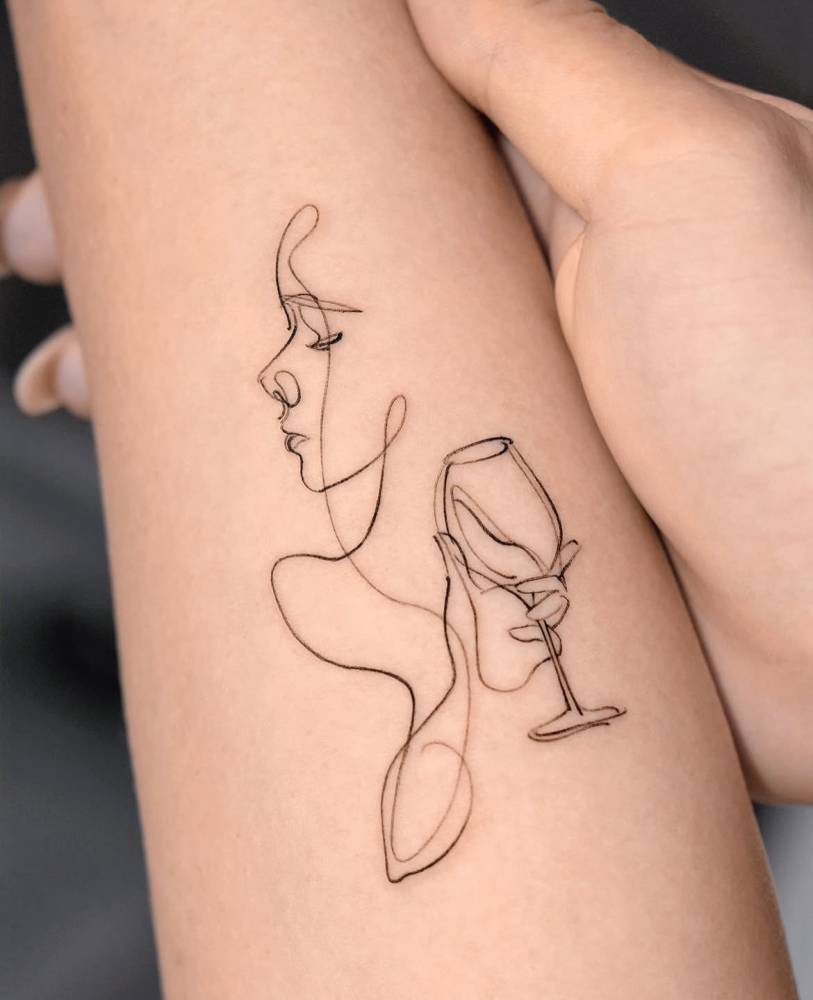 Sketch work style woman drinking wine tattoo located on the inner forearm.