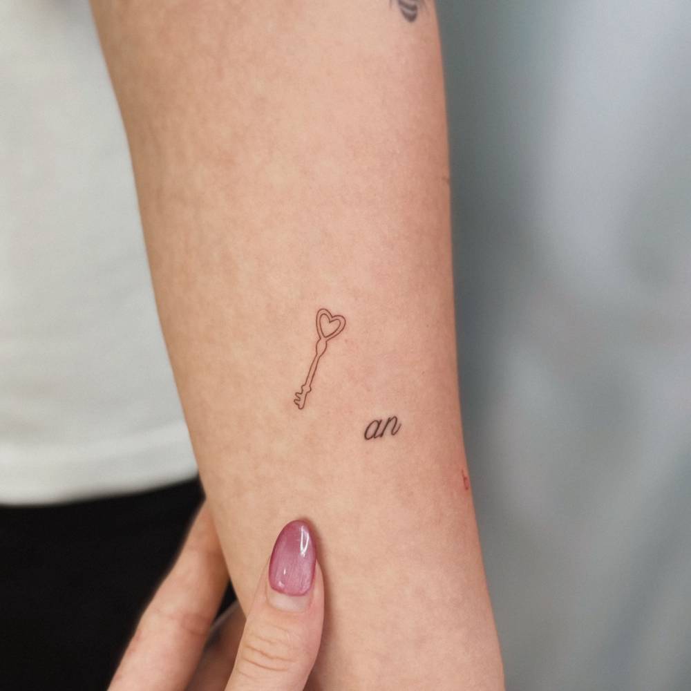Tiny fine line style heart key tattoo located on the forearm.