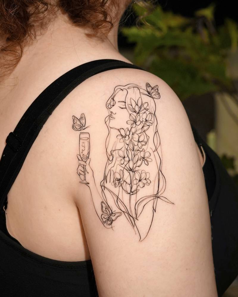 Flower head woman drinking wine tattooed on the shoulder.