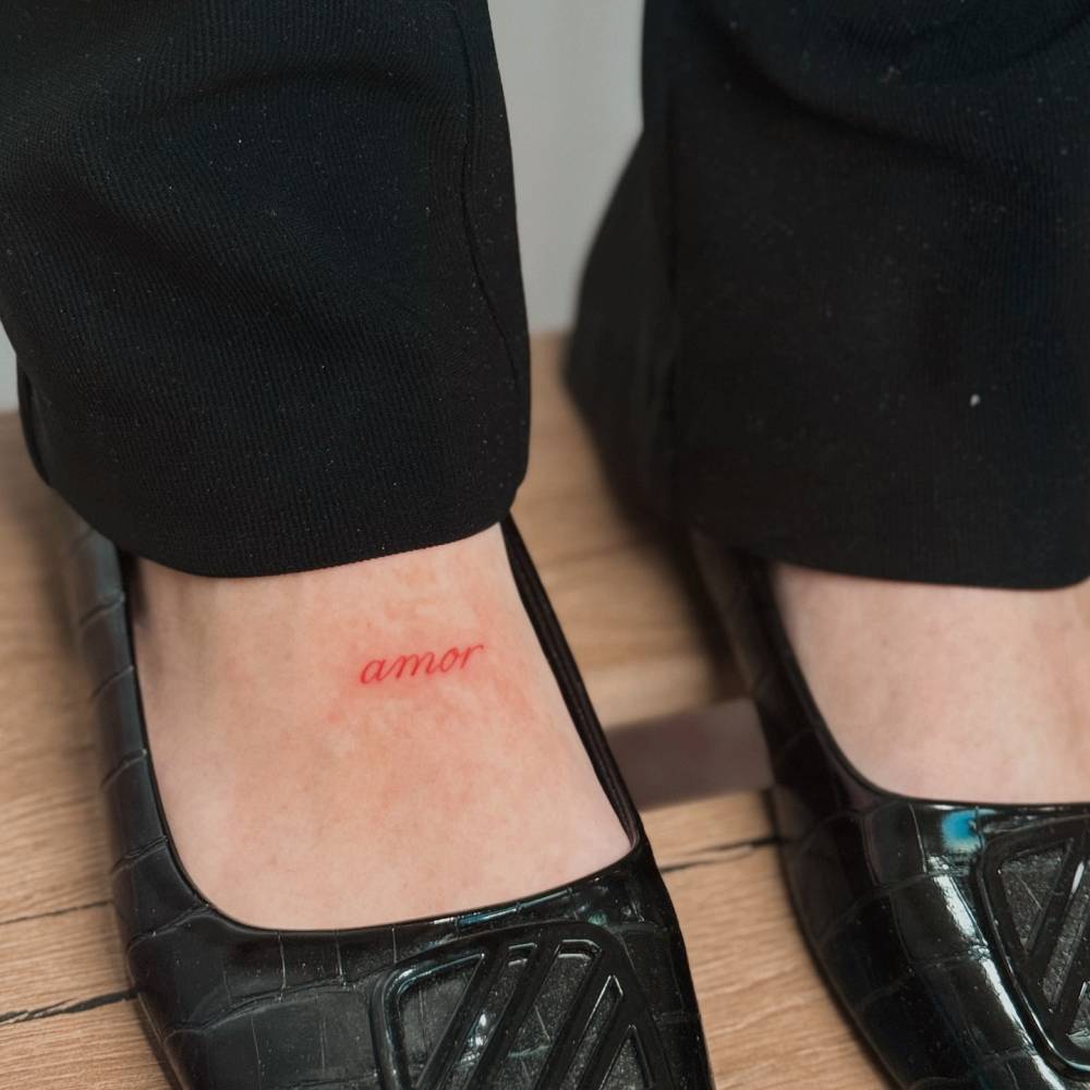 Tattoo of the word "amor" in red ink located on the foot.