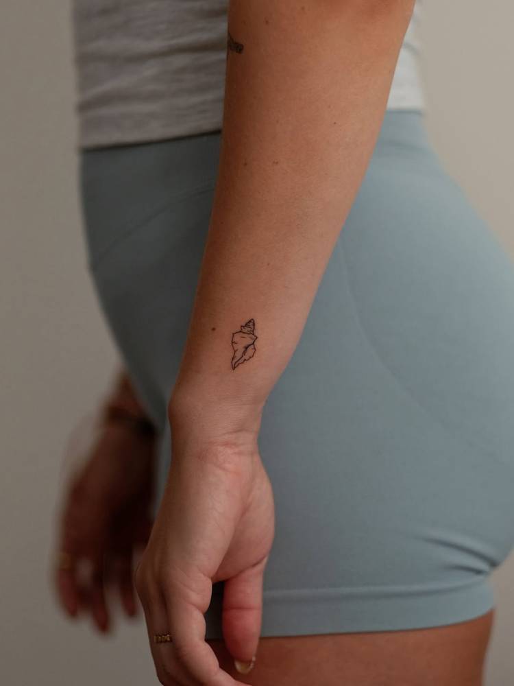 Tiny minimalistic tulip shell tattoo located on the wrist.