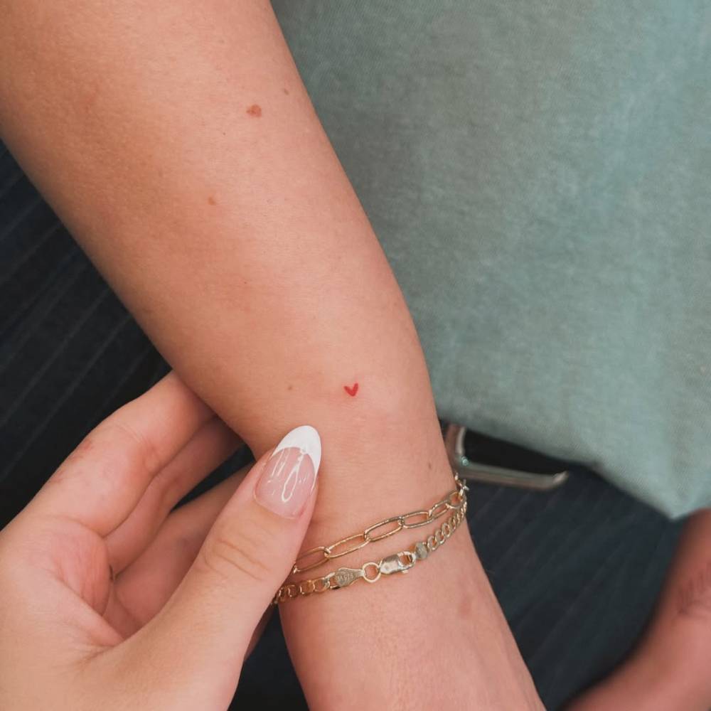 Tiny red heart tattoo in minimalistic style placed on the wrist.