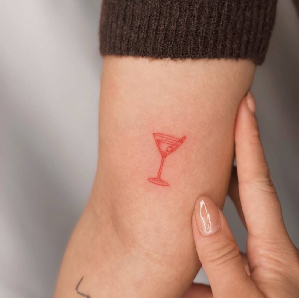 Fine line style martini cocktail tattoo in red ink placed on the inner arm.