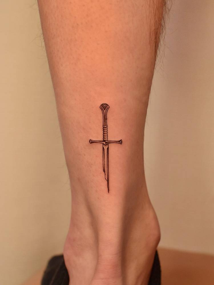 Broken sword tattoo in fine line style located on the achilles.
