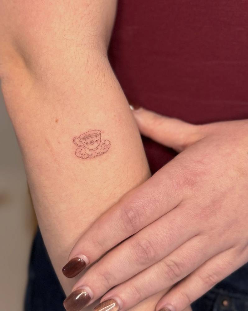Tiny teacup tattoo located on the forearm, done in fine line style.