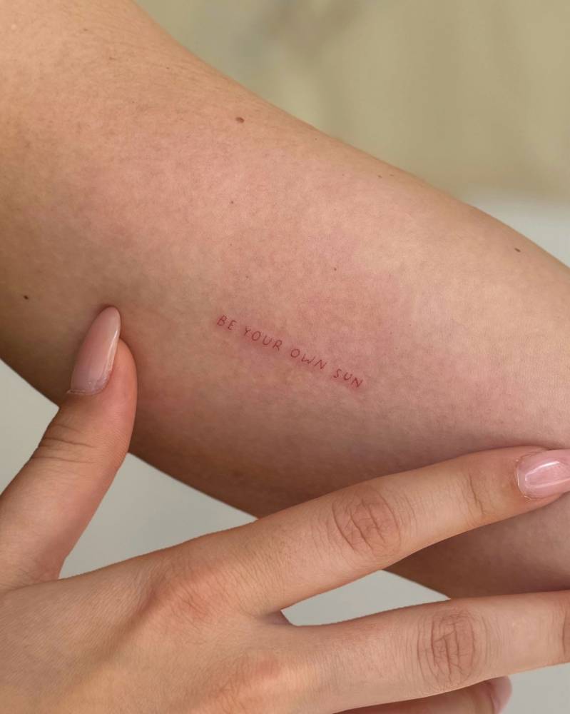 Handwritten font "be your own sun" lettering tattoo done on the inner arm.