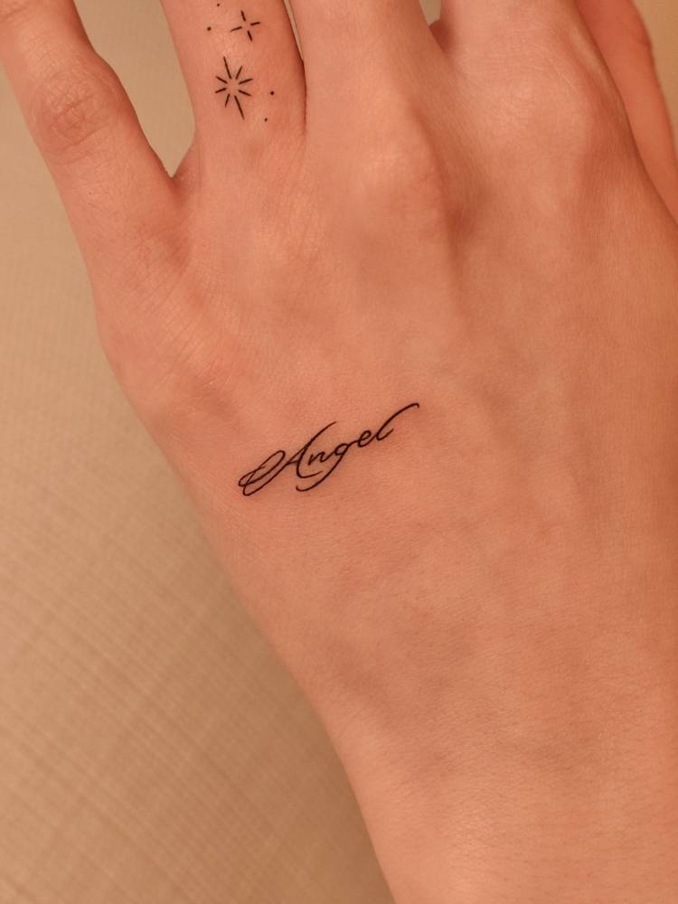 Word "angel" in handwritten font tattooed on the hand.