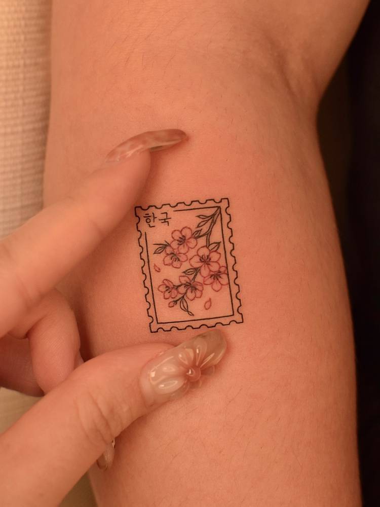 Cherry blossom stamp tattoo located on the forearm, fine line style.