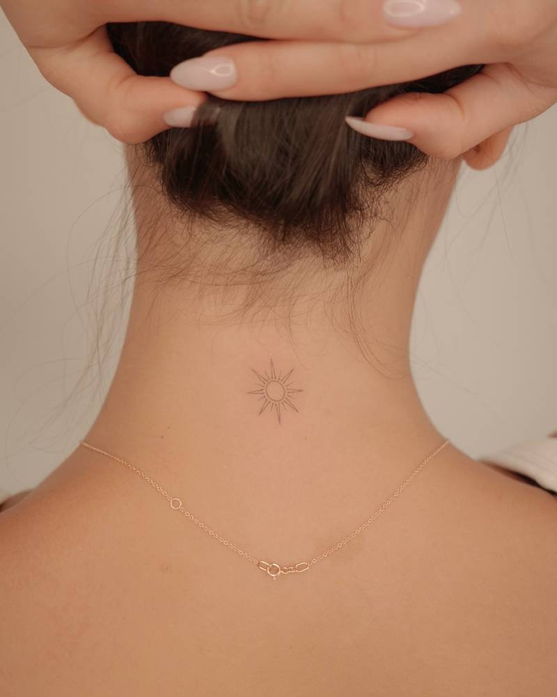 Fine line style little sun tattoo located on the back of the neck.