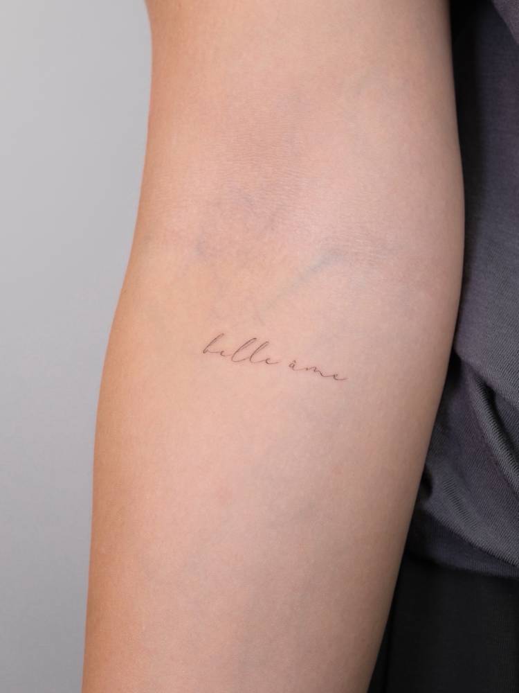 "Belle âme" lettering tattoo located on the inner forearm.