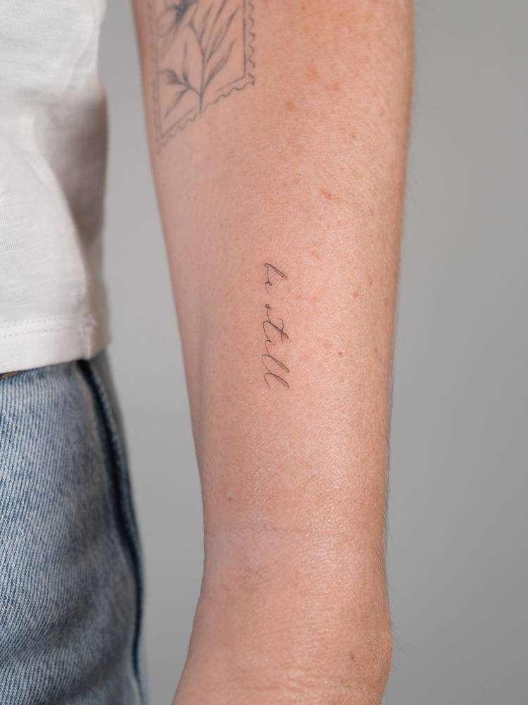 Handwritten font lettering tattoo that says "be still" located on the wrist.