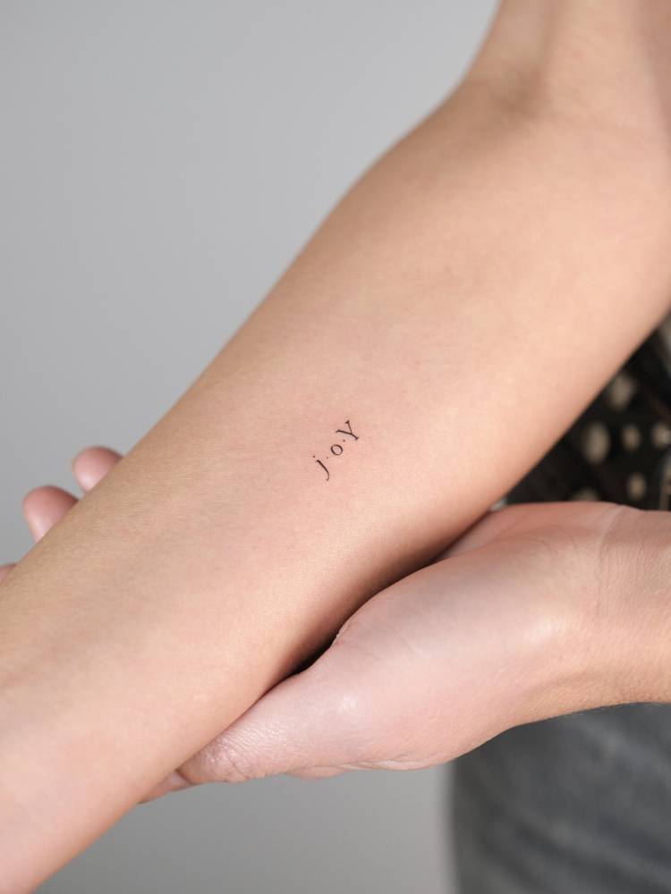 Little tattoo of the word "joy" in serif font placed on the inner forearm.