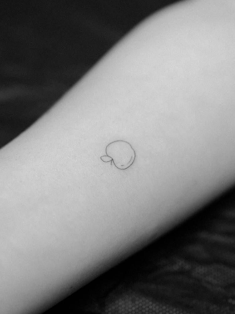 Tiny apple tattoo in fine line style located on the inner forearm.