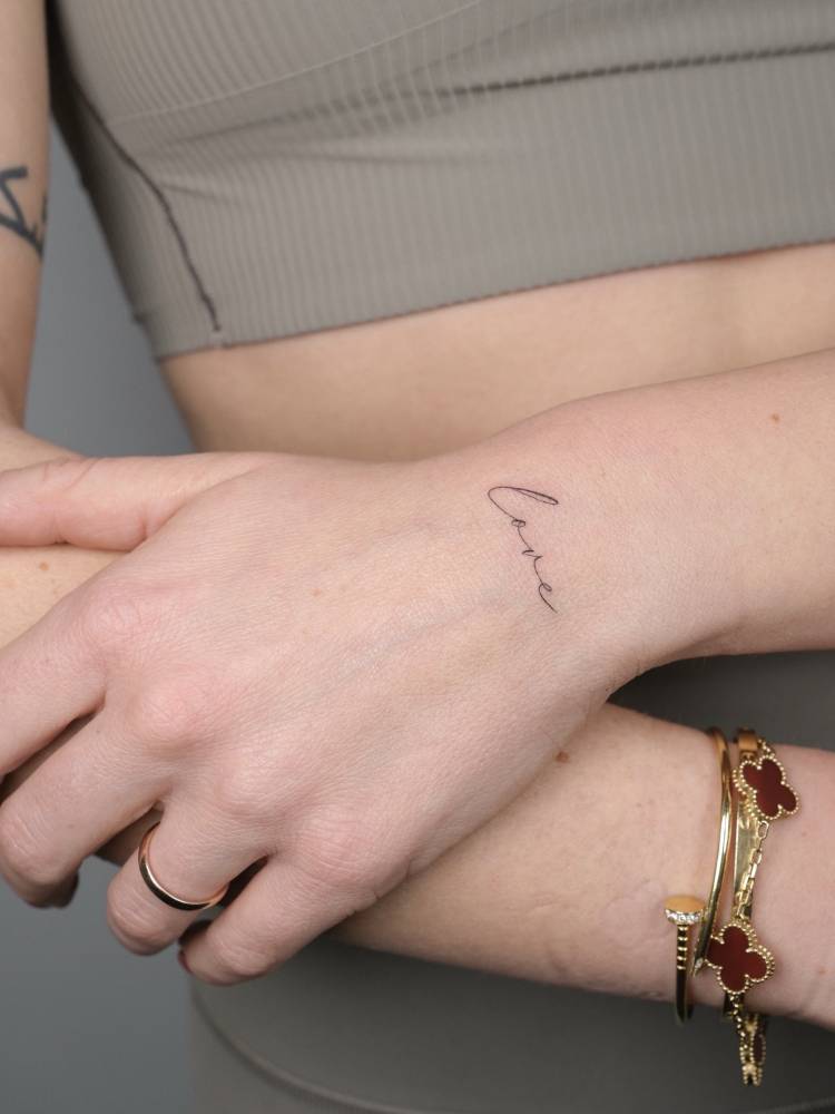 Script font word "love" tattooed on the wrist.