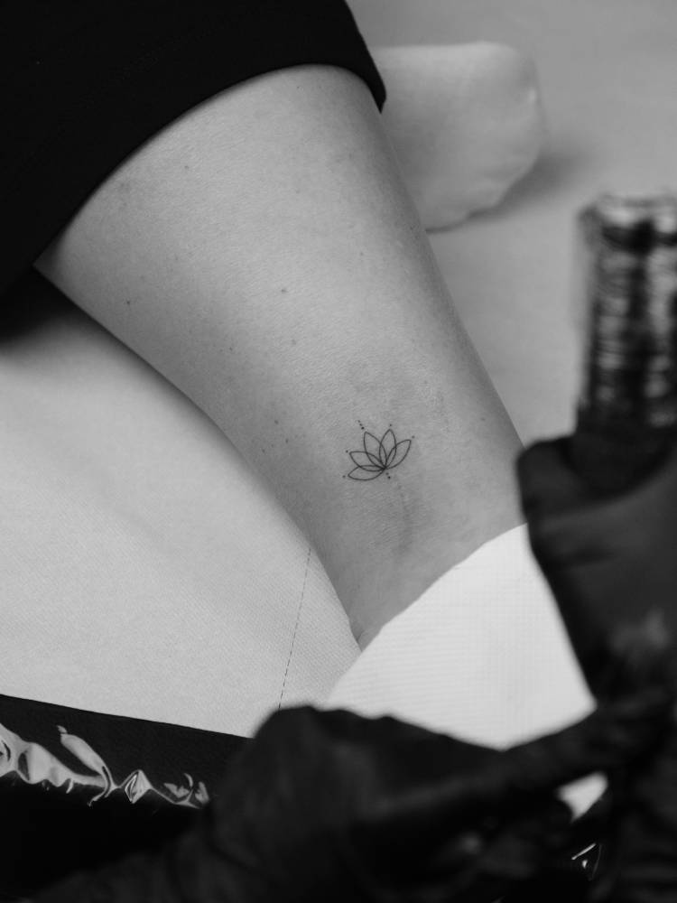 Small lotus flower tattoo in fine line style done on the ankle.