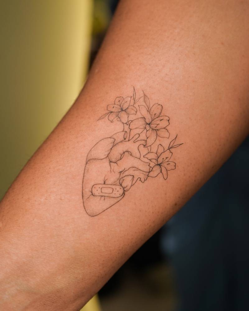 Anatomical heart and flowers tattoo located on the forearm.