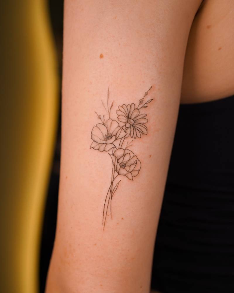 Fine line style flower bouquet tattoo located on the tricep.