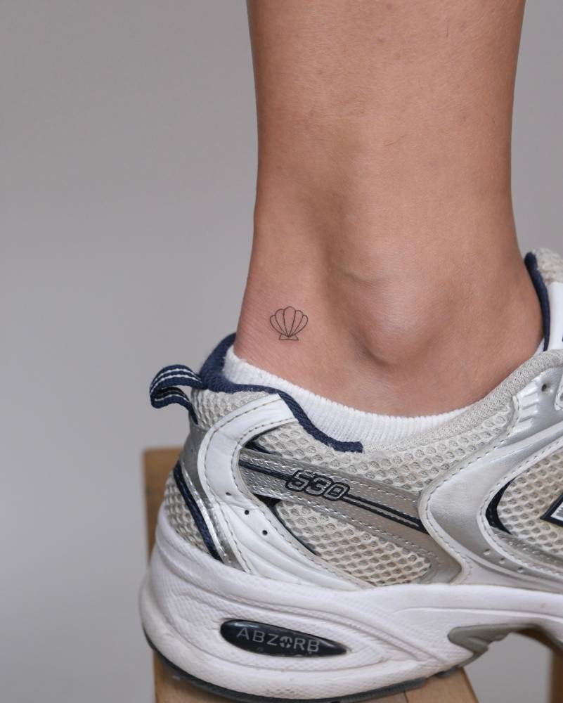 Micro scallop shell tattoo located on the ankle, minimalistic style.