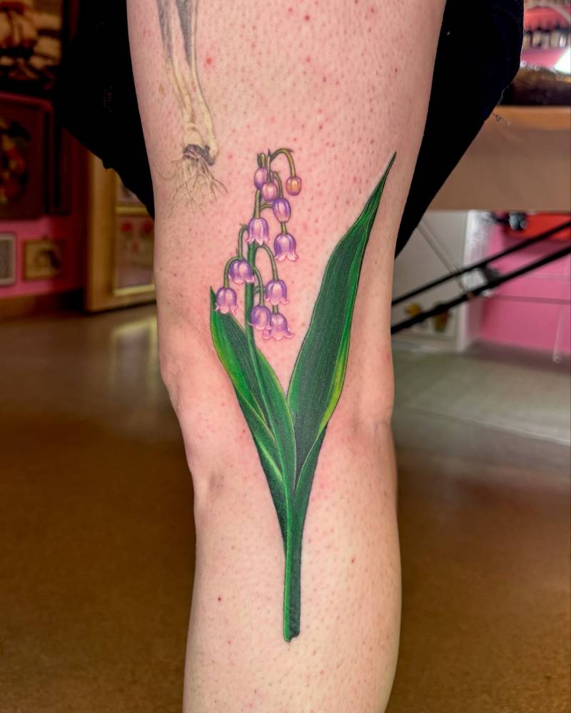Lily of the valley flowers tattooed on the leg, done in illustrative style.