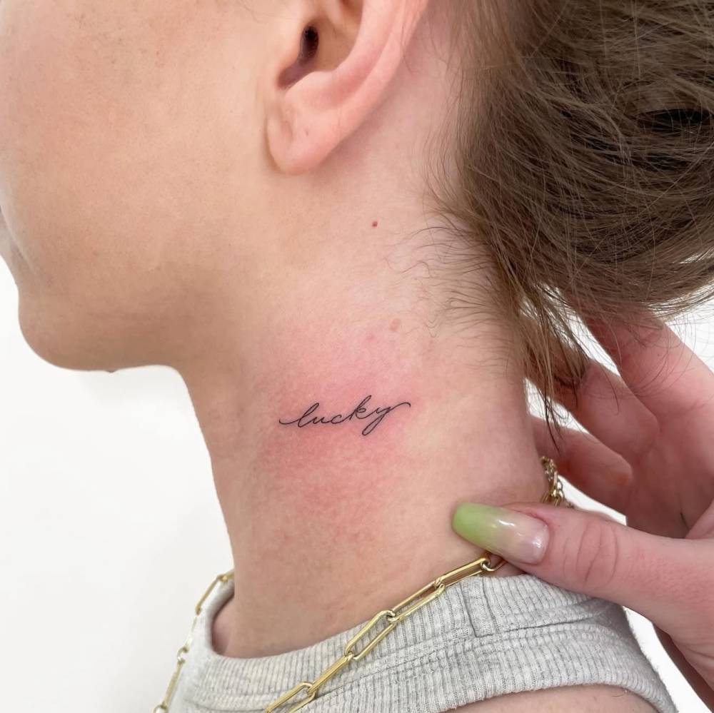 Handwritten font word "lucky" tattooed on the neck.