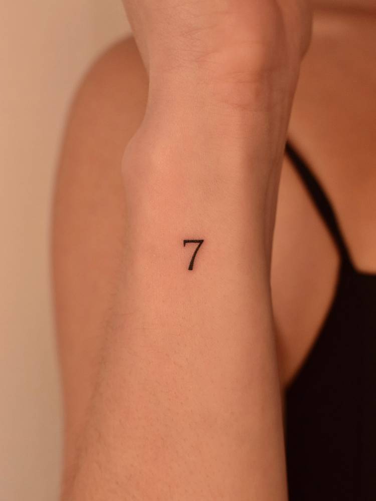 Tiny minimalistic number "7" tattooed on the wrist.