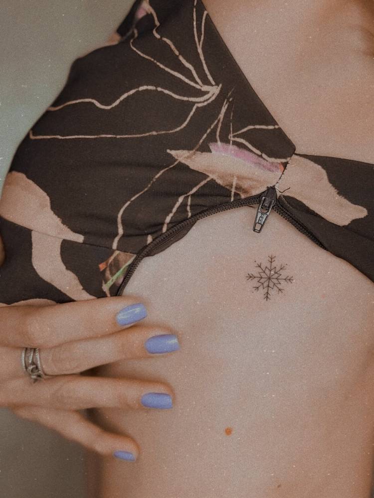 Fine line style snowflake tattoo located on the side boob.