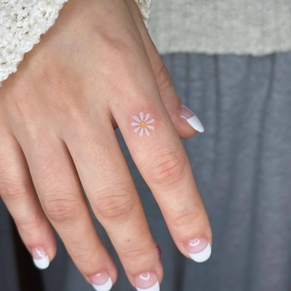 Hand poked daisy flower tattoo located on the finger.