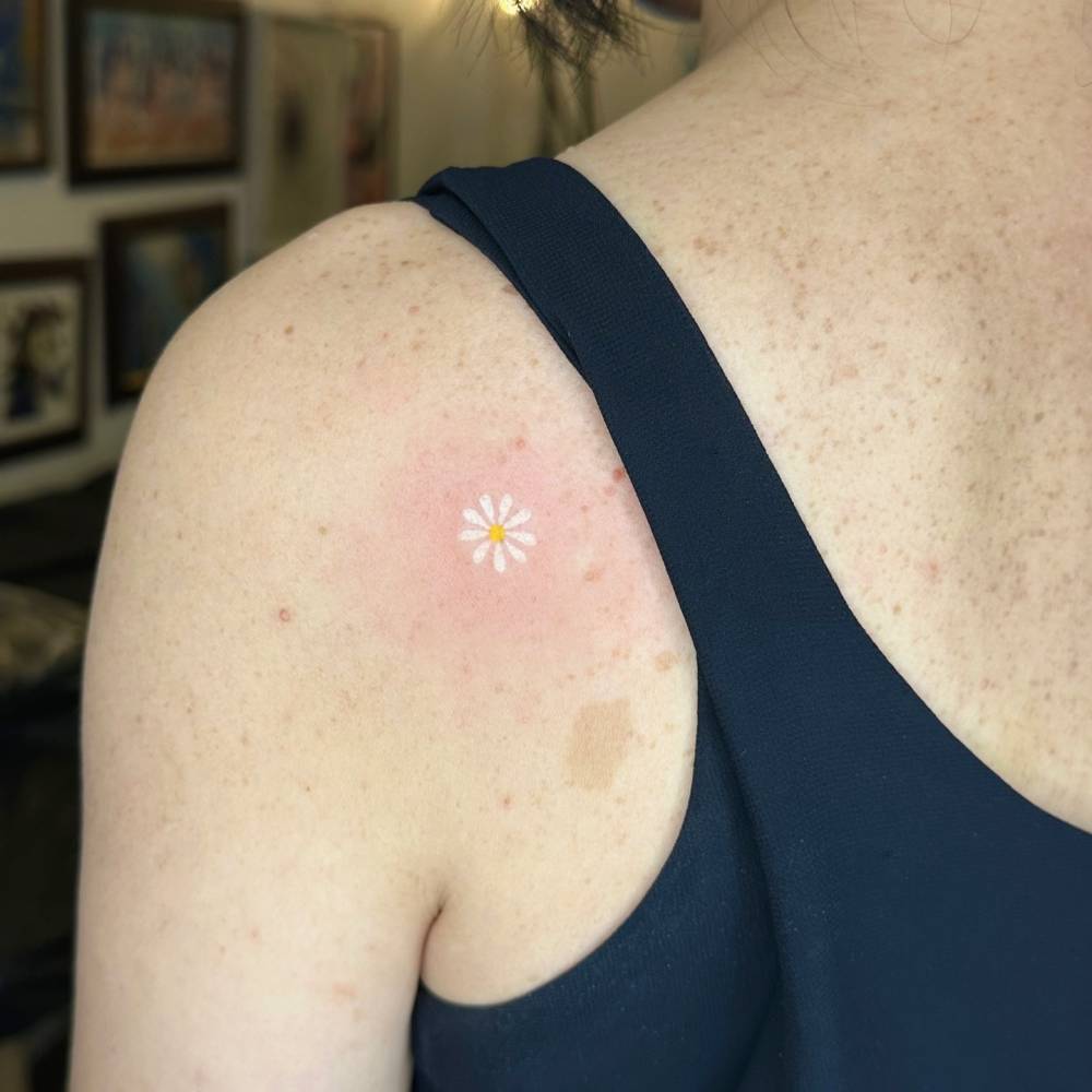 Hand poked daisy flower tattoo located on the shoulder blade.