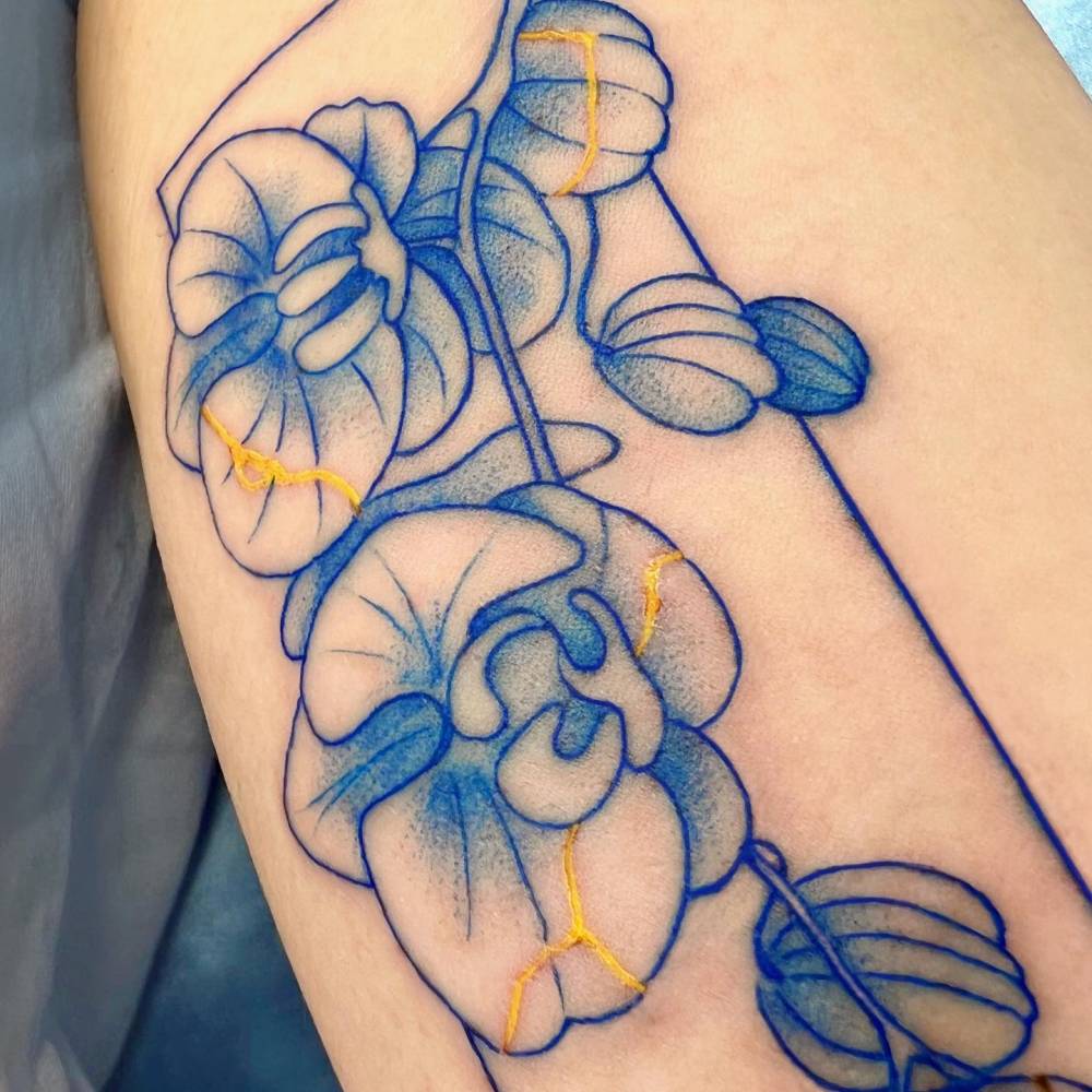 Blue kintsugi orchid tattoo located on the inner arm.